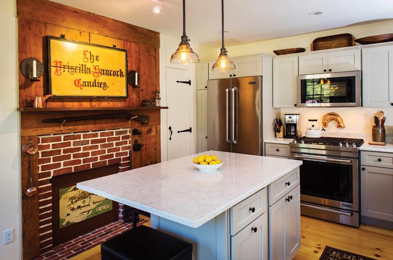 Modern cabinetry mixes with a nineteenth-century fireplace, vintage Island signs, and a painting of the home by Ted Meinelt .