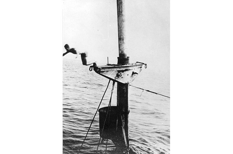 Teenage boy diving from the mast of the submerged Port Hunter, circa 1940.